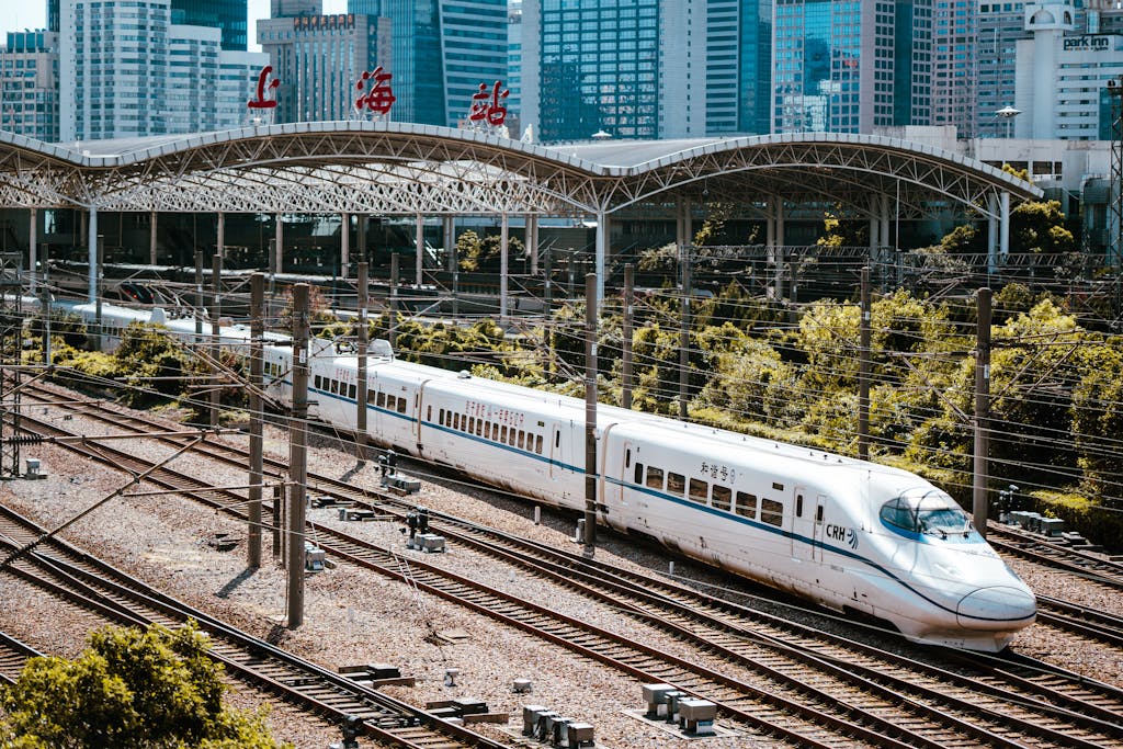A high-speed train passing through Shanghai Railway Station with city skyline in the background.