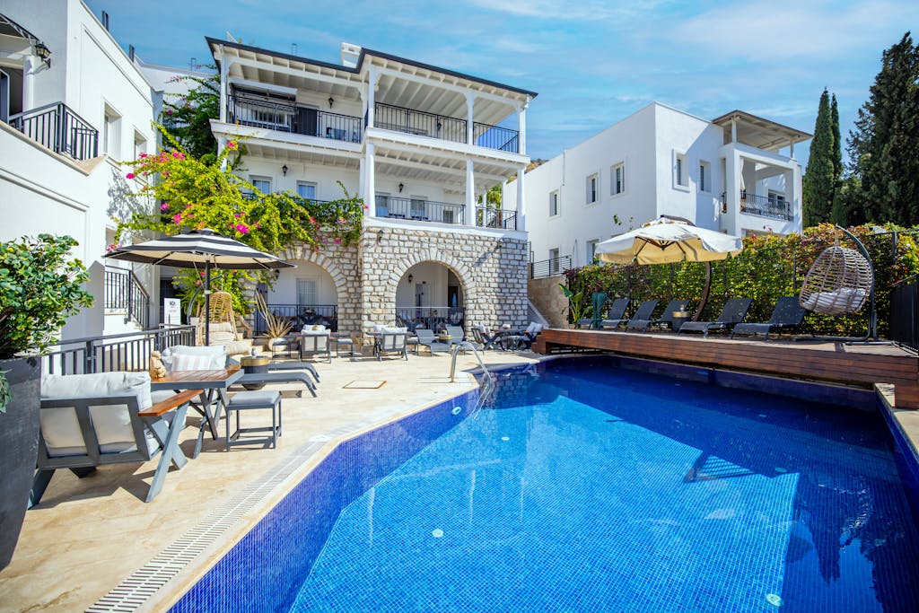 Lavish villa in Bodrum with poolside seating and vibrant greenery under a sunny sky.