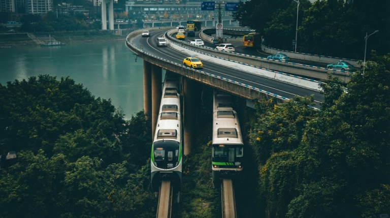 A vertical shot of Chongqing's "8D" transportation system, featuring two CRT monorail trains running on tracks directly beneath a curving highway overpass filled with yellow taxis and cars.