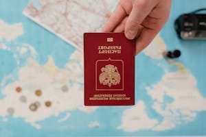 A hand holding a Russian passport over a map, suggesting travel preparation.